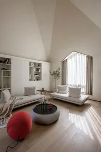 A minimalist living room with neutral-toned furniture, large windows, and a low round table.