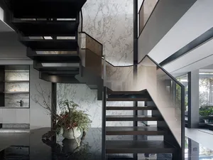 A modern minimalist staircase with black metal and marble steps, glass railings, and a potted plant nearby.