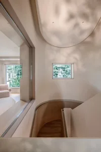 A minimalist staircase with wooden walls and floor, featuring a small window and a curved handrail.