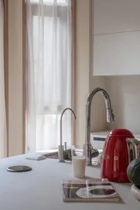 Modern minimalist kitchen featuring metal, glass, and a red plastic kettle on the countertop near a window with sheer curtain