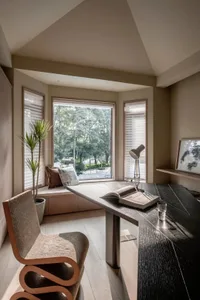 A modern minimalist home office space featuring a sleek wooden desk, glass windows, and a comfortable seating area with natur