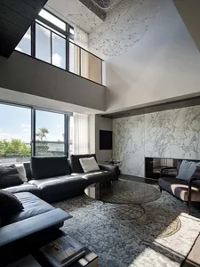 A modern living room featuring marble finishes and glass elements, with large windows and a high ceiling.