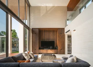 Well-lit modern living room featuring a sectional sofa, coffee table, large windows, and a wooden accent wall with a mounted 