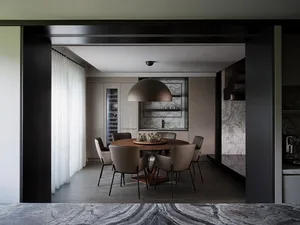 A modern dining room with a round table, chairs, and a large marble countertop.
