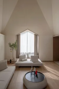 A minimalist living room featuring neutral-toned furniture and decor, with a large arched window allowing natural light to fi