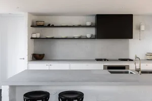 A modern, minimalist kitchen features concrete countertops and an open shelving system.