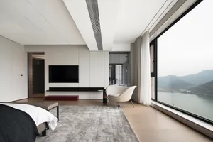 Modern bedroom with minimalist decor, white walls, floor-to-ceiling windows overlooking mountains, and wooden flooring.