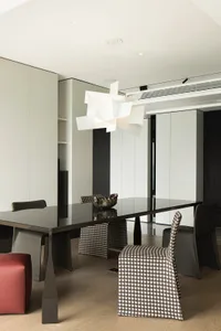 A modern dining room featuring patterned chairs and a sleek, black dining table, illuminated by a contemporary light fixture.