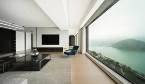 Modern minimalist living room with large glass window overlooking water, featuring a black marble coffee table and a blue arm