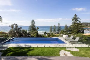A modern poolside view featuring glass walls and a blue infinity pool with a clear blue sky above.