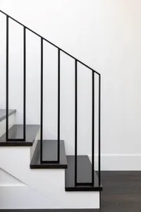 A modern staircase with black railings against a white wall