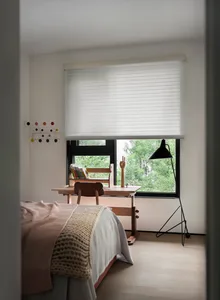 A minimalist bedroom with wooden furniture, a bed, a desk, and a window with greenery outside.