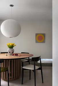 Modern dining room with wooden table, pendant light, yellow tulips, and apples on a plate.