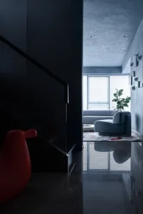 A modern living room featuring a concrete-terrazzo flooring with a sleek black staircase, a red modern chair, and a cozy seat