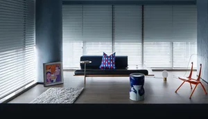 A modern living room with a concrete floor, wooden furniture, and horizontal blinds on the windows.