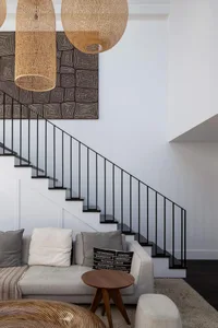 Modern living room featuring a contemporary staircase with black metal railing, a woven pendant light, a white sectional sofa
