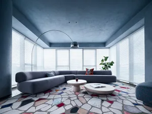 A modern living room featuring a gray L-shaped sectional sofa, a patterned rug, and a circular coffee table with books and a 