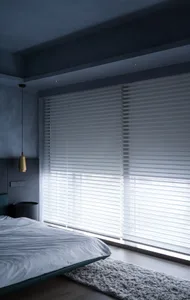 A modern minimalist bedroom with silk blinds, a cozy rug, and a sleek bed.