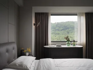 A modern minimalist bedroom featuring textured curtains, marble furniture, and a large window overlooking lush greenery.