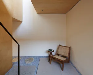 Minimalist interior space with wooden chair, concrete floor, and stone accents.