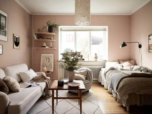 A cozy Scandinavian-style bedroom with light pink walls, wooden floors, and a mix of soft textures and natural materials.
