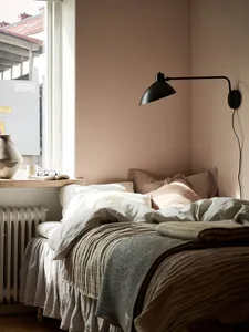 Minimalist bedroom with light-colored walls, window, and bed with natural textiles, featuring a wall-mounted lamp and a book 