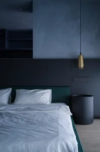 Minimalist bedroom with a white bed, green headboard, and a black bedside table with a lamp.