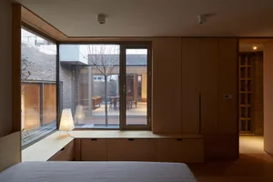 A minimalist bedroom with wooden cabinets and a large window overlooking a courtyard.