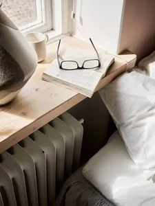 A minimalist bedroom featuring a wooden table with a book, glasses, and a mug.