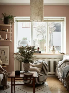 A minimalistic living room with organic materials, featuring a striped armchair, a wooden table, and a window with a plant.