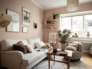 A living room with minimalist decor, featuring a white sofa, striped armchair, and pink walls with framed artwork.
