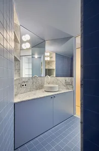 A modern bathroom with white terrazzo flooring, blue tiles, and a white countertop with a circular sink.