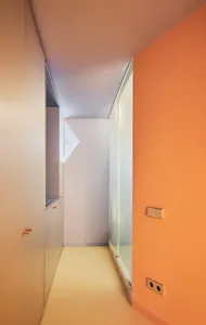 Modern corridor with orange and white walls, glass door, and wooden cabinets.