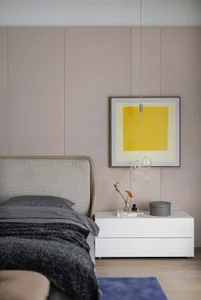 Modern minimalist bedroom featuring a fabric upholstered bed, wooden nightstand, glass vase with flowers, and abstract art.
