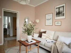 A living room with neutral-toned walls, a white sofa, a wooden coffee table with a vase of flowers, and framed pictures on th