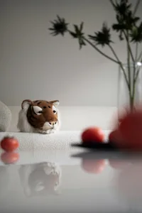 A stuffed tiger head resting on a white couch with a potted plant nearby.
