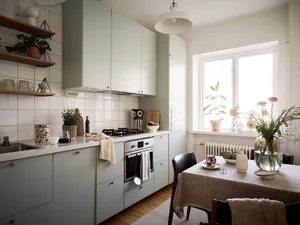 Modern kitchen with green cabinets, white tiles, and wooden flooring.