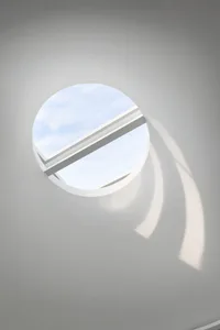 Circular skylight with metal frame on a white ceiling, casting light and shadows.