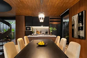A modern residential kitchen with a wooden finish, featuring a dining table and chairs, a kitchen island with a marble backsp