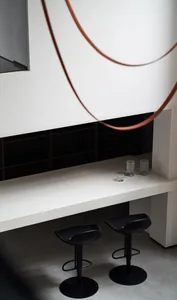 Bar counter with minimalist design, black stools, and decorative glasses on a white concrete surface.