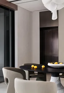 A minimalist residential dining area featuring a black table with a bowl of lemons and a white marble base.