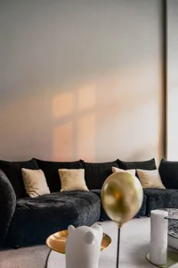 A modern minimalistic living room featuring a black velvet sofa with white cushions, a gold metallic balloon, and a white cer