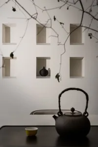 A minimalist tea ceremony setup featuring a black teapot and teacup on a reflective surface, with a wall displaying decorativ
