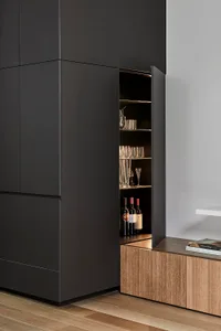 A modern black laminate kitchen cabinet with a wooden bottom cabinet displaying bottles and glasses.