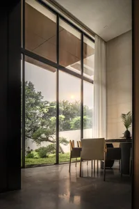 Modern dining room featuring glass walls and cement flooring with a large window overlooking a lush garden.