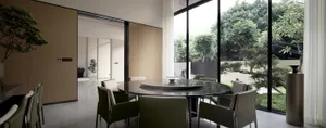 Modern dining room featuring a round marble table surrounded by chairs, with large windows providing a view of a green outdoo