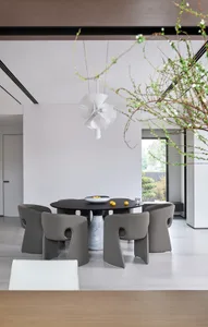 Modern dining room interior with minimalist black dining table, grey chairs, and a white flower arrangement.