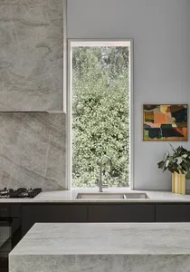 A modern kitchen with marble countertops and a large window overlooking greenery.