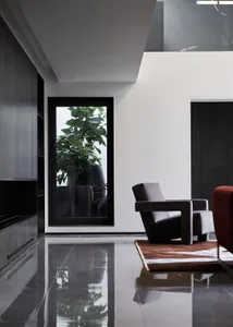 A minimalist modern living room with a sleek dark armchair, a rug, and sleek dark wooden cabinetry with a tall window display