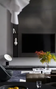 A modern living room with mixed materials features a dark TV wall, minimalist furniture, and a vibrant floral arrangement on 